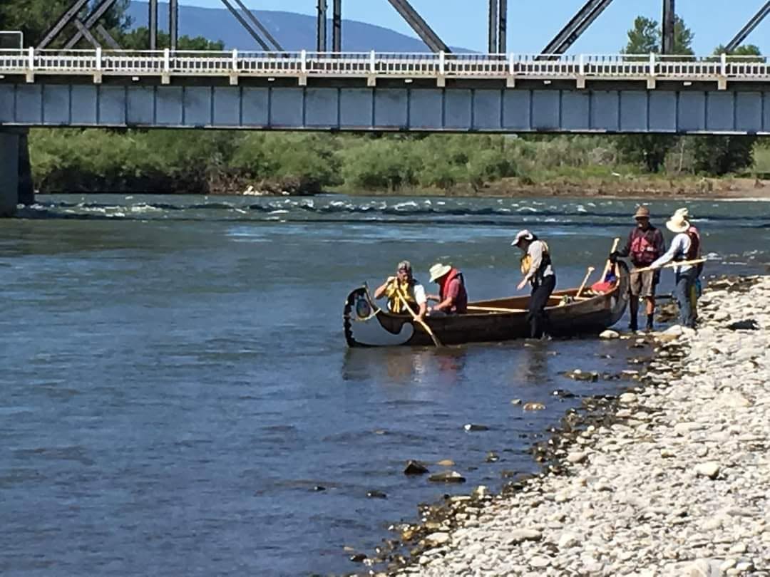 Two CVBS paddlers in traditional voyageur costume standing beside decorated big canoes on the Athabasca River