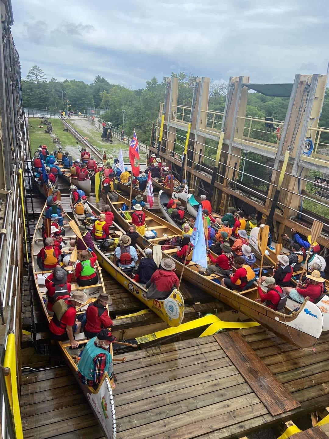 Two voyageur canoes packed with paddlers on open water flying Saskatchewan and Alberta provincial flags